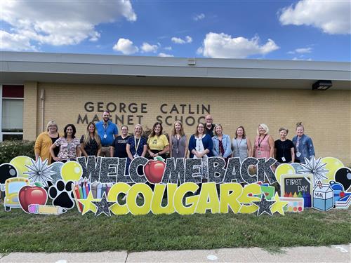 The Catlin Arts Staff is pictured in front of a large yard sign that says "Welcome Back Cougars"