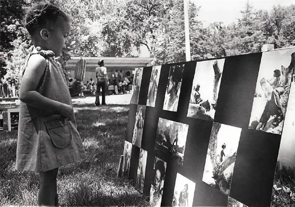 A young black girl looks at a collage of pictures at a park