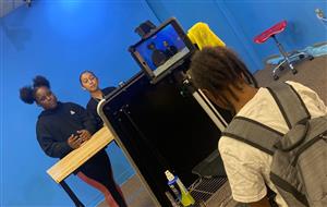 Three Students film in front of a blue wall