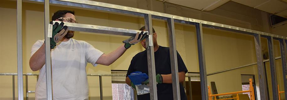 A student places metal into a frame while a teacher watches